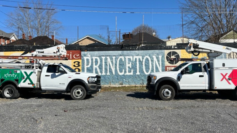 Two Xfinity trucks parked near mural featuring Princeton.
